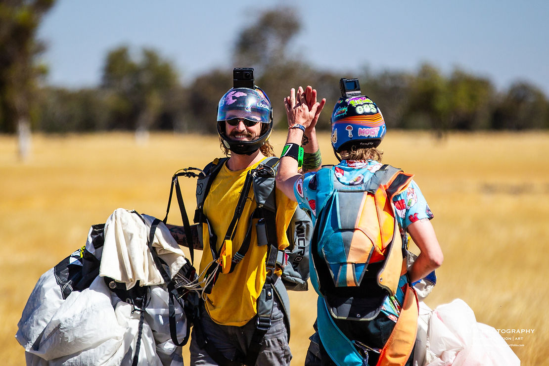 Two skydivers high five after landing in paddock