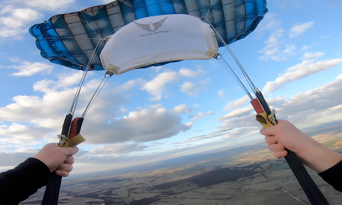 a parachute with white slider opening under blue and cloudy sky