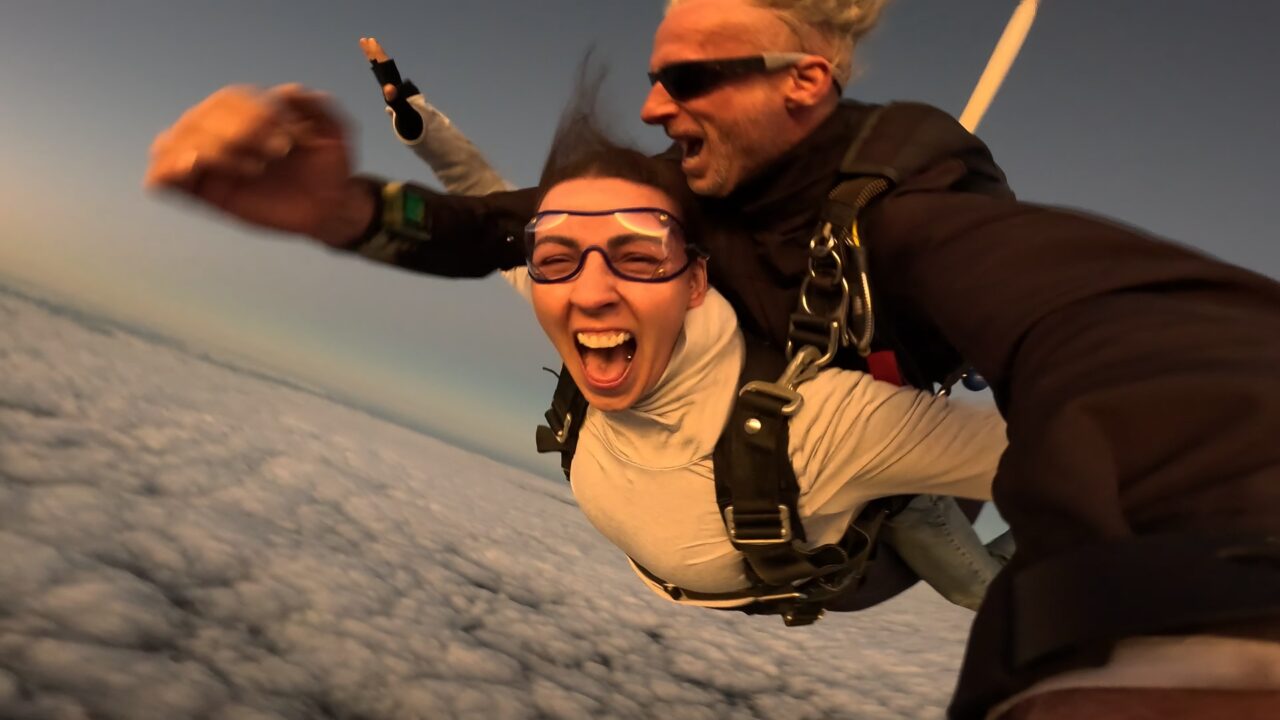 Tandem skydiver yelling with excitement in freefall with her instructor above the clouds in WA