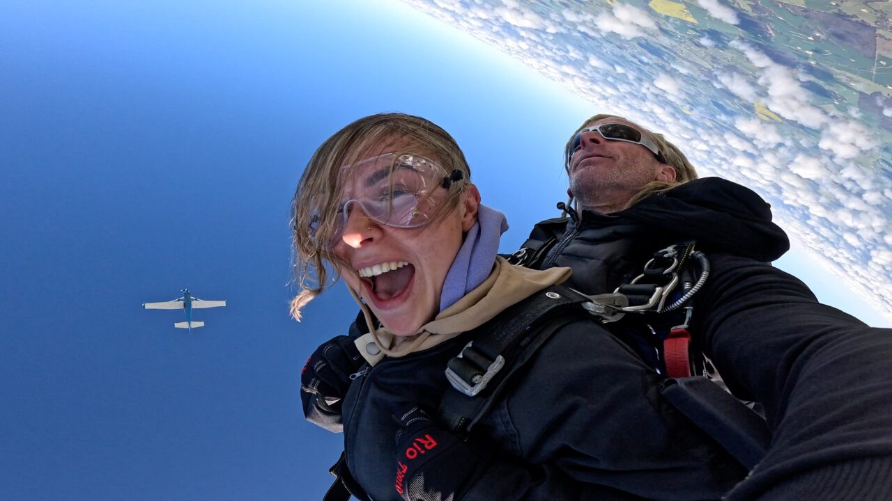 Tandem skydiver yelling with joy in freefall with her instructor, the jump plane behind them, near Bunbury WA