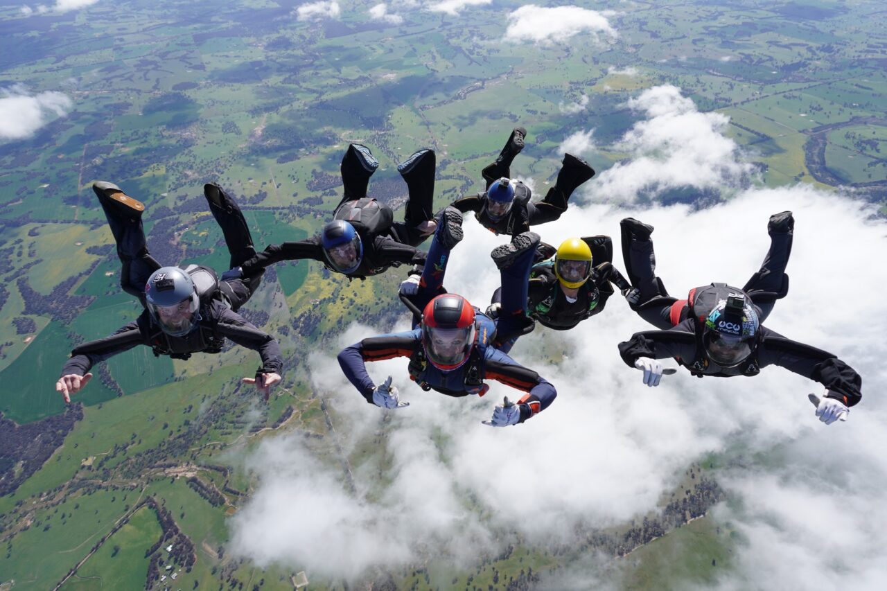 Six skydivers holding a formation in freefall above the clouds