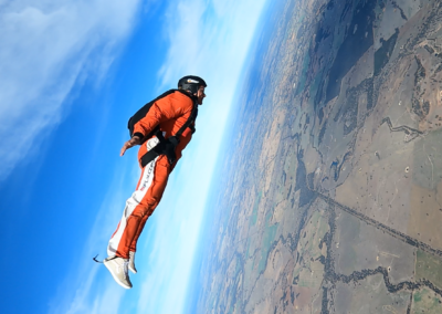 A solo skydiver in an orange jumpsuit performing a tracking flight over the Western Australia landscape.