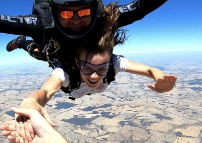 A female tandem skydiving student smiling during freefall over Western Australia near Perth.
