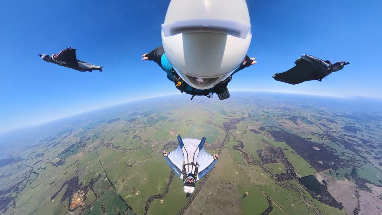 Four skydivers in a wingsuit formation gliding over the Western Australia landscape at Hillman Farm