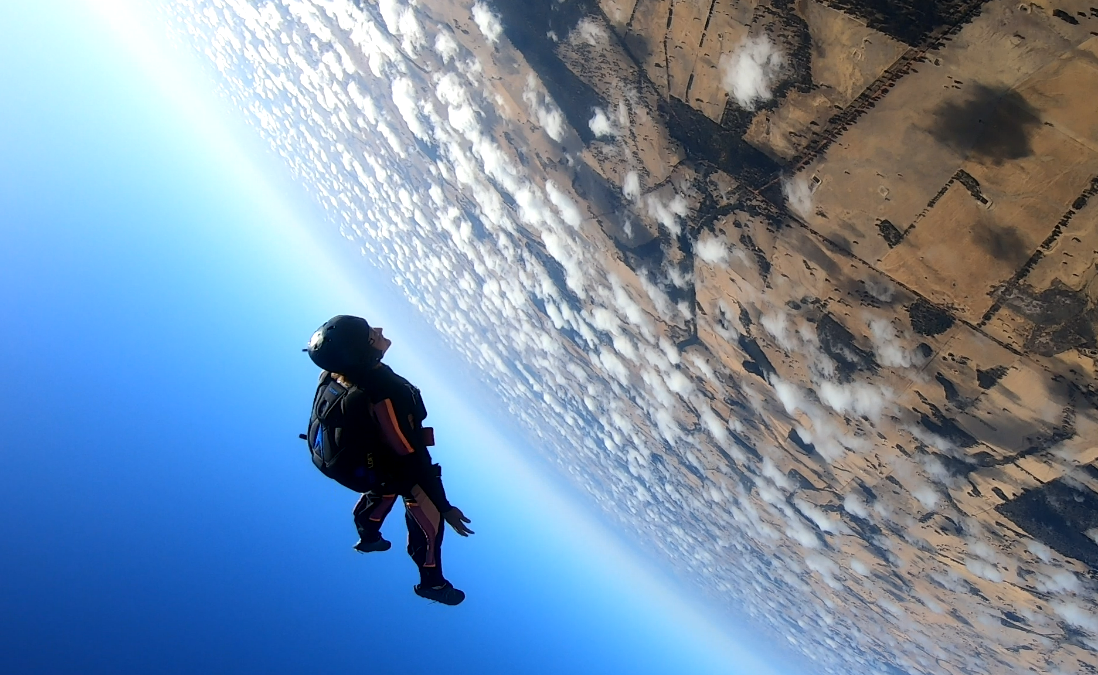 A solo skydiver in freefall high above the clouds and the curve of the earth